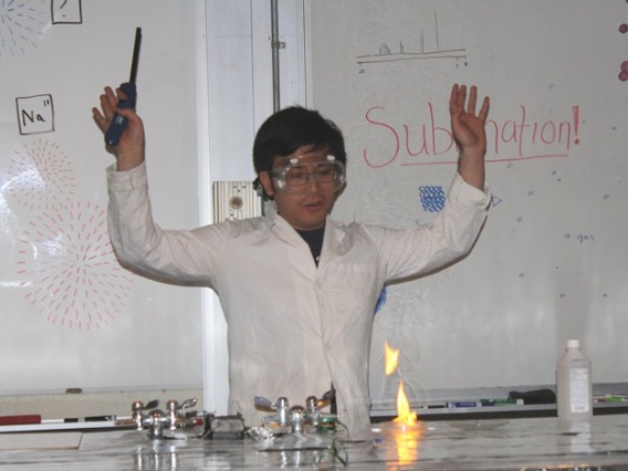 Student in lab coat and goggles performing an experiment with a flame