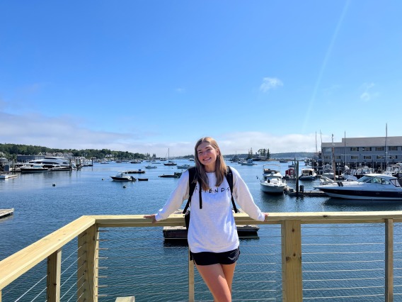 Ellie Rottier smiling while standing on a pier overlooking a large body of water with multiple boats