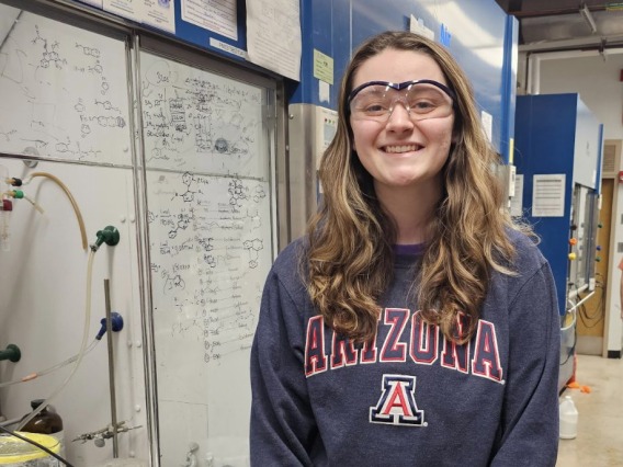 Ashley Wellik smiling for the camera while standing in a lab near a whiteboard