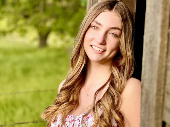 Marley Novak smiling at the camera while outside leaning back against a wooden barn
