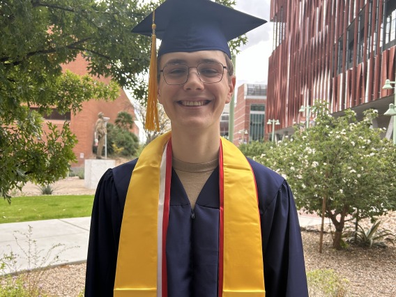 Caleb Seekins stands with large smile in cap and gown