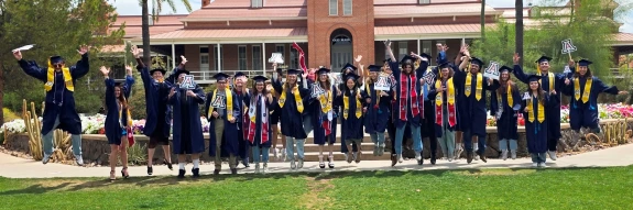 2025 CBC Graduates Jumping in Cap and Gown in front of Old Main (not all graduates are pictured)