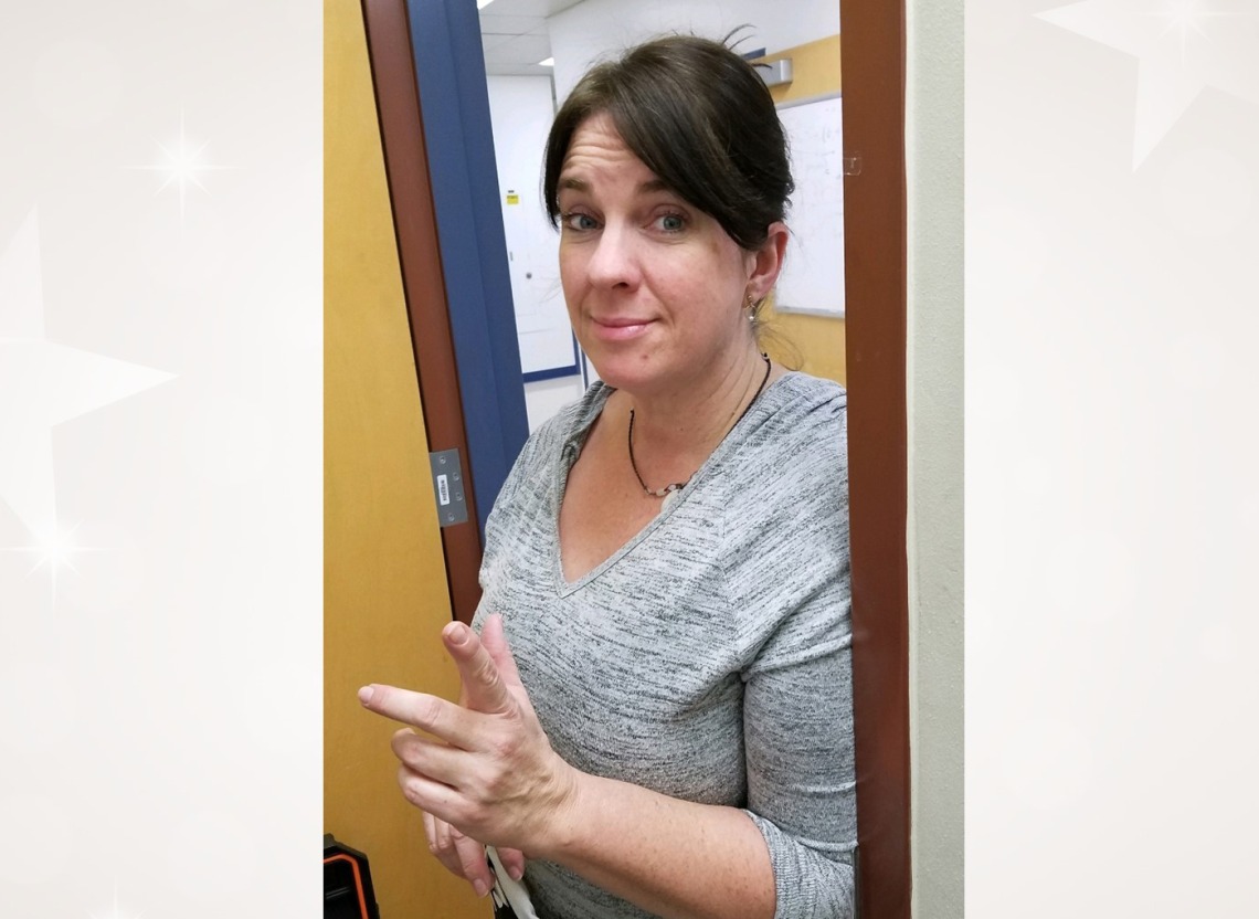 Jennifer Autz in a doorway with a hand gesture similar to a peace sign